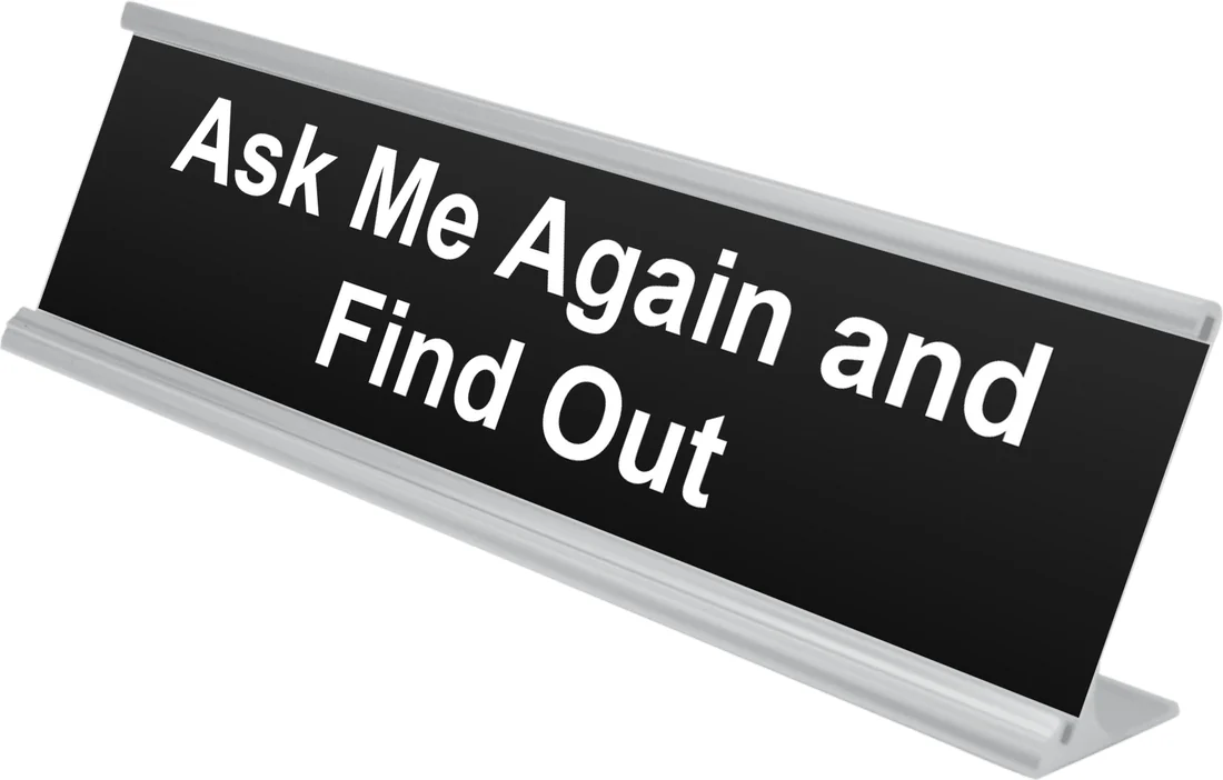 Ask Me Again and Find Out desk plate in black, shown in an aluminum desk holder
