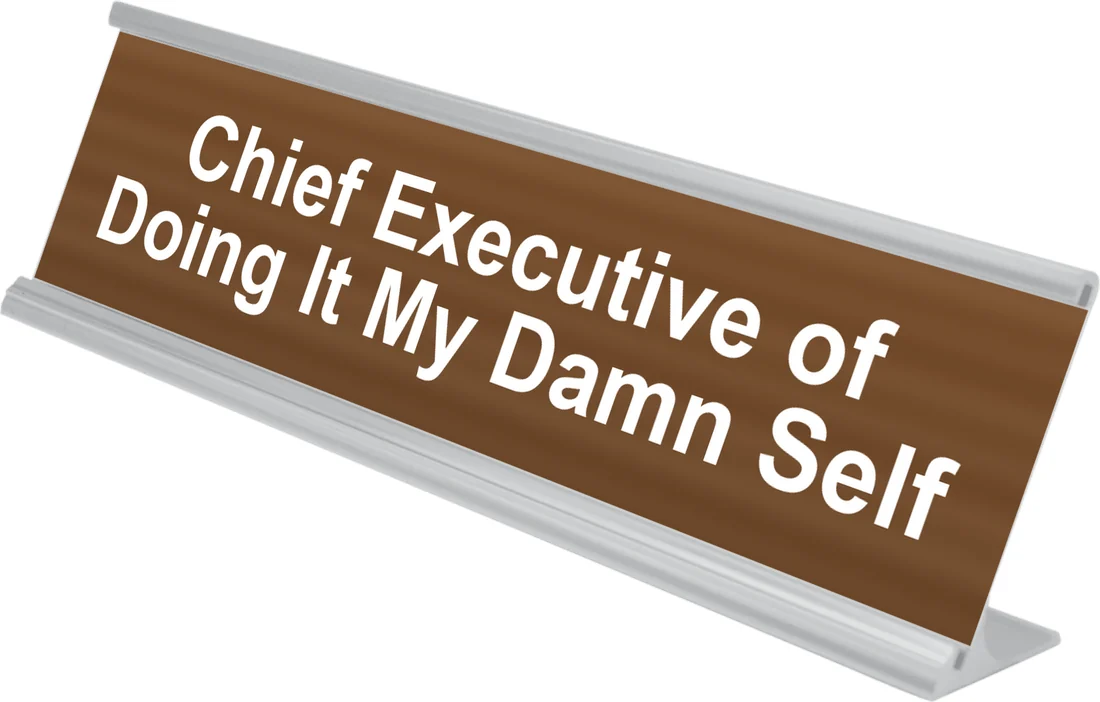 Chief Executive of Doing It My Damn Self desk plate in walnut, shown in an aluminum desk holder