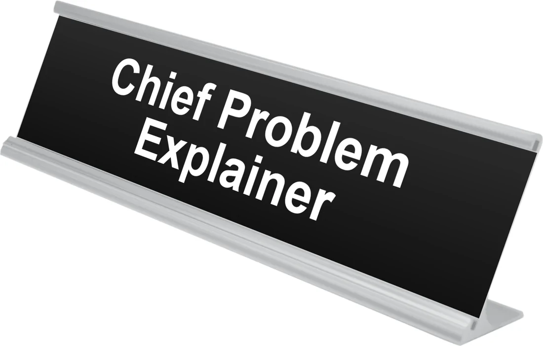 Chief Problem Explainer desk plate in black, shown in an aluminum desk holder