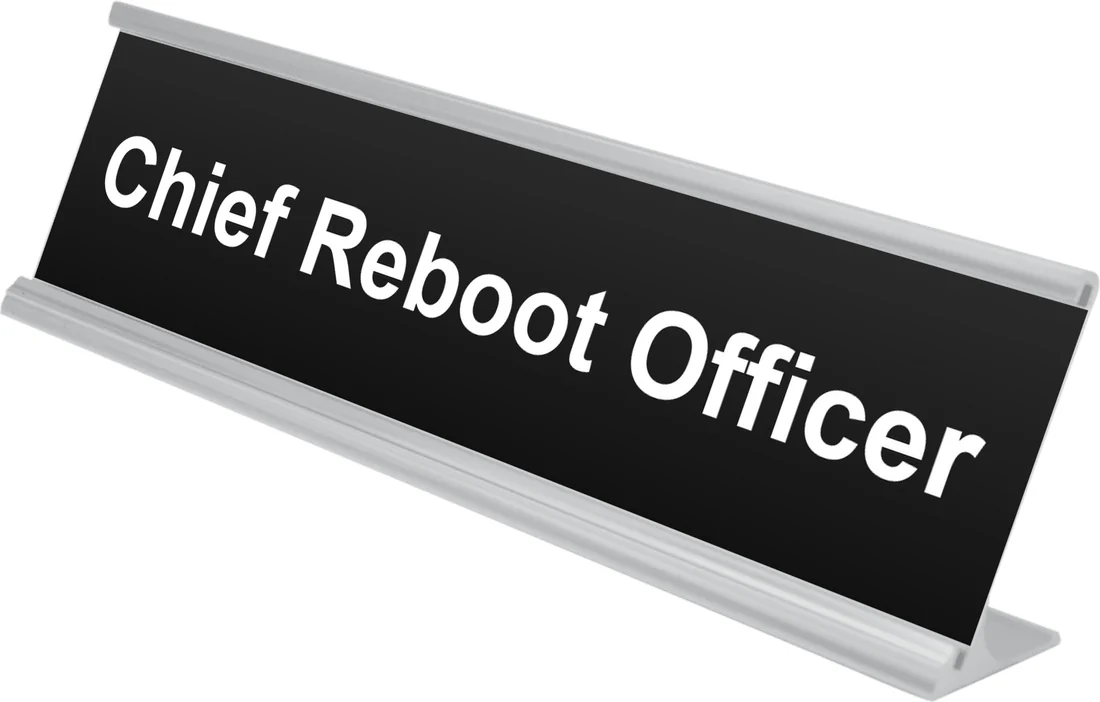 Chief Reboot Officer desk plate in black, shown in an aluminum desk holder