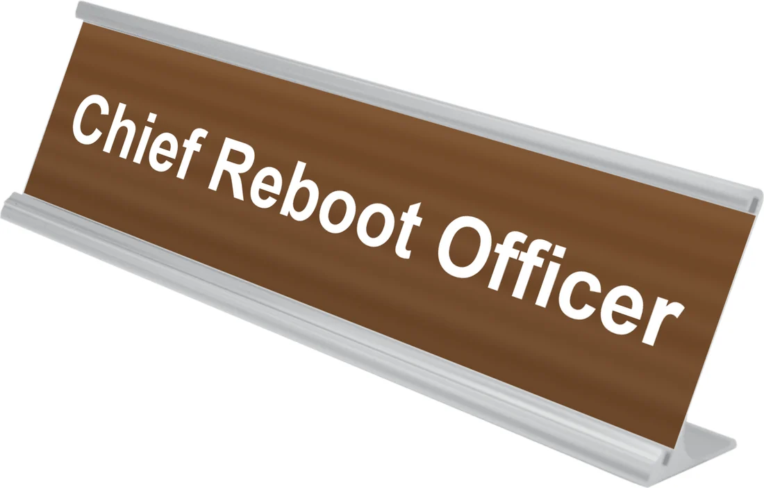 Chief Reboot Officer desk plate in walnut, shown in an aluminum desk holder