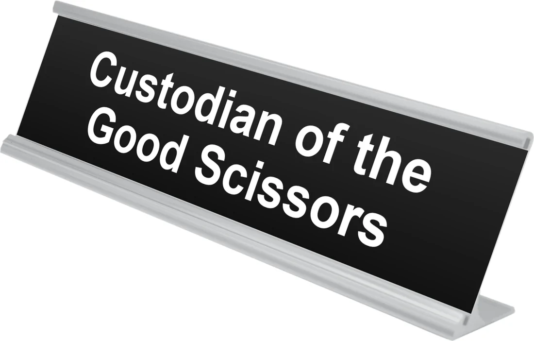Custodian of the Good Scissors desk plate in black, shown in an aluminum desk holder
