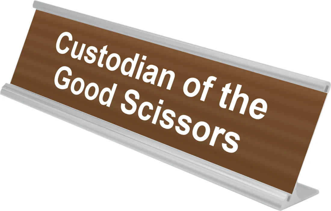 Custodian of the Good Scissors desk plate in walnut, shown in an aluminum desk holder
