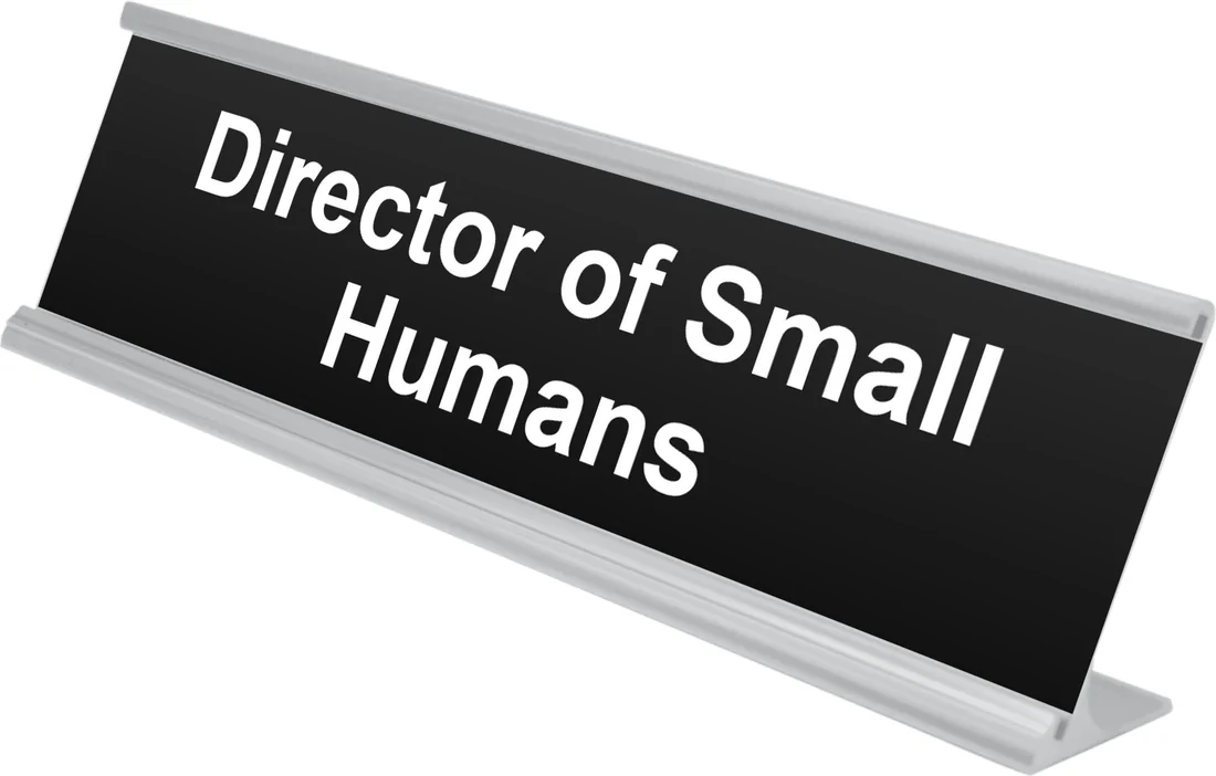 Director of Small Humans desk plate in black, shown in an aluminum desk holder