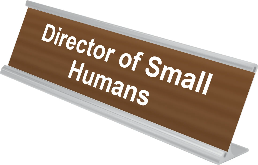 Director of Small Humans desk plate in walnut, shown in an aluminum desk holder
