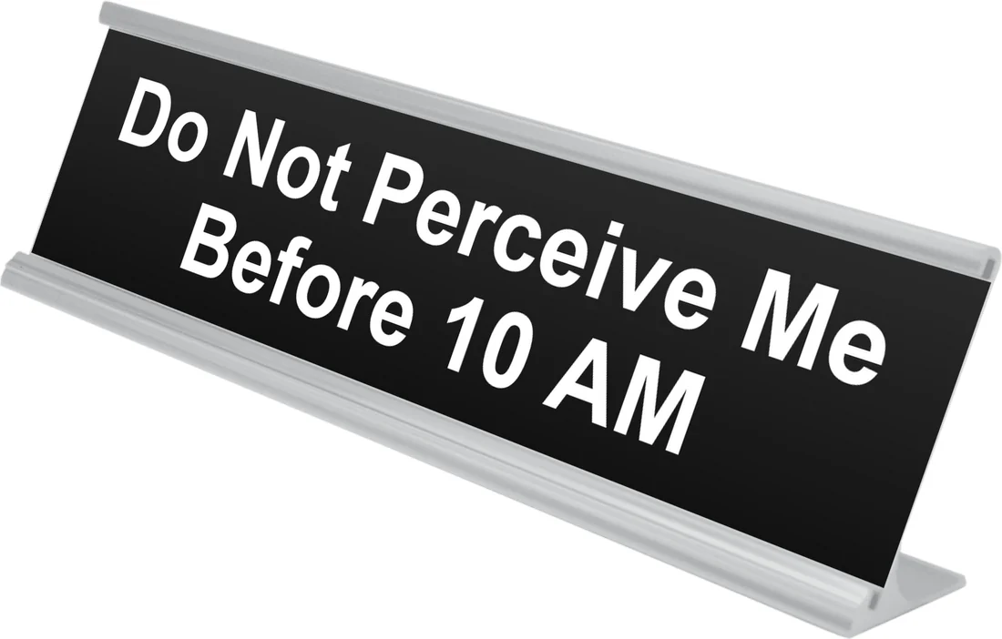Do Not Perceive Me Before 10 AM desk plate in black, shown in an aluminum desk holder