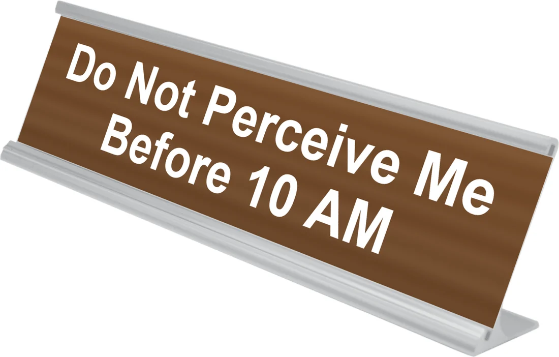 Do Not Perceive Me Before 10 AM desk plate in walnut, shown in an aluminum desk holder