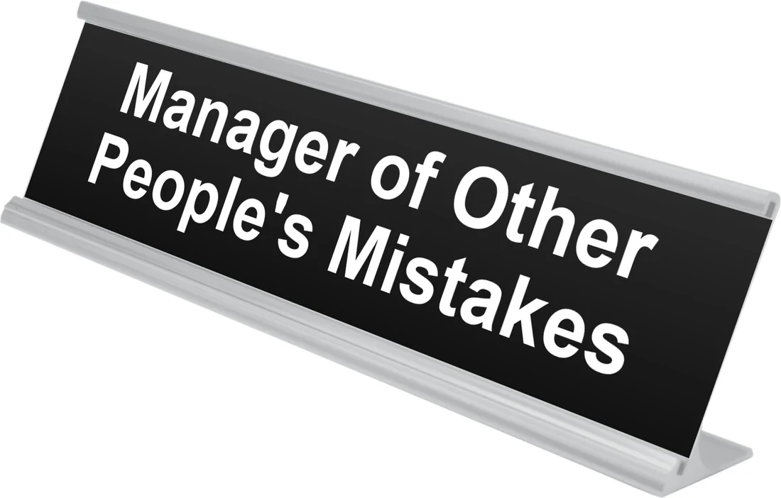 Manager of Other People's Mistakes desk plate in black, shown in an aluminum desk holder