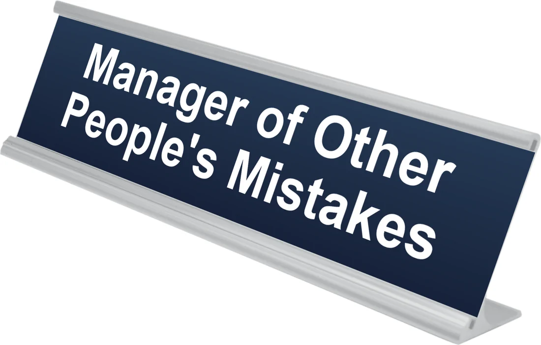 Manager of Other People's Mistakes desk plate in navy, shown in an aluminum desk holder