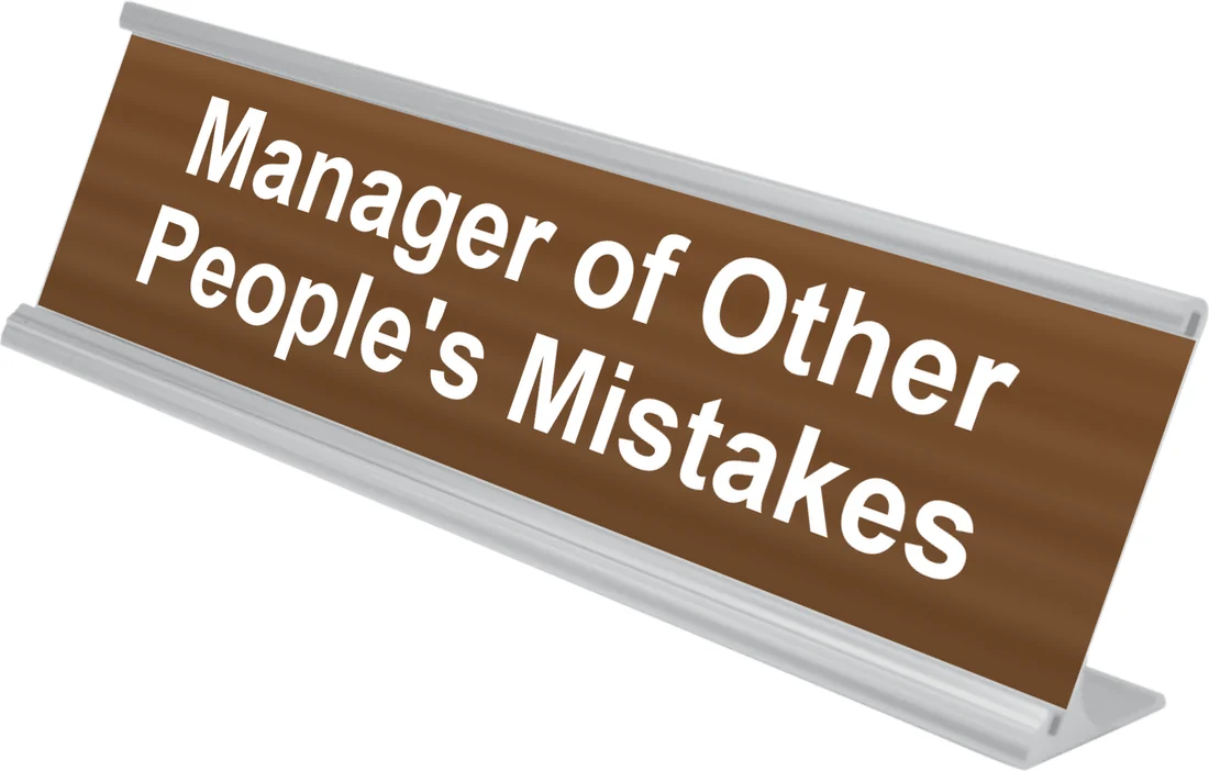 Manager of Other People's Mistakes desk plate in walnut, shown in an aluminum desk holder