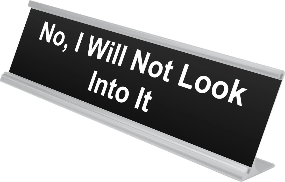 No, I Will Not Look Into It desk plate in black, shown in an aluminum desk holder