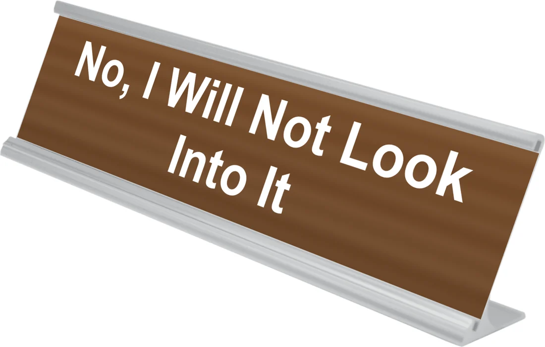 No, I Will Not Look Into It desk plate in walnut, shown in an aluminum desk holder