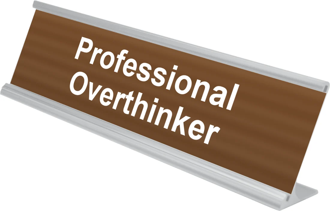 Professional Overthinker desk plate in walnut, shown in an aluminum desk holder