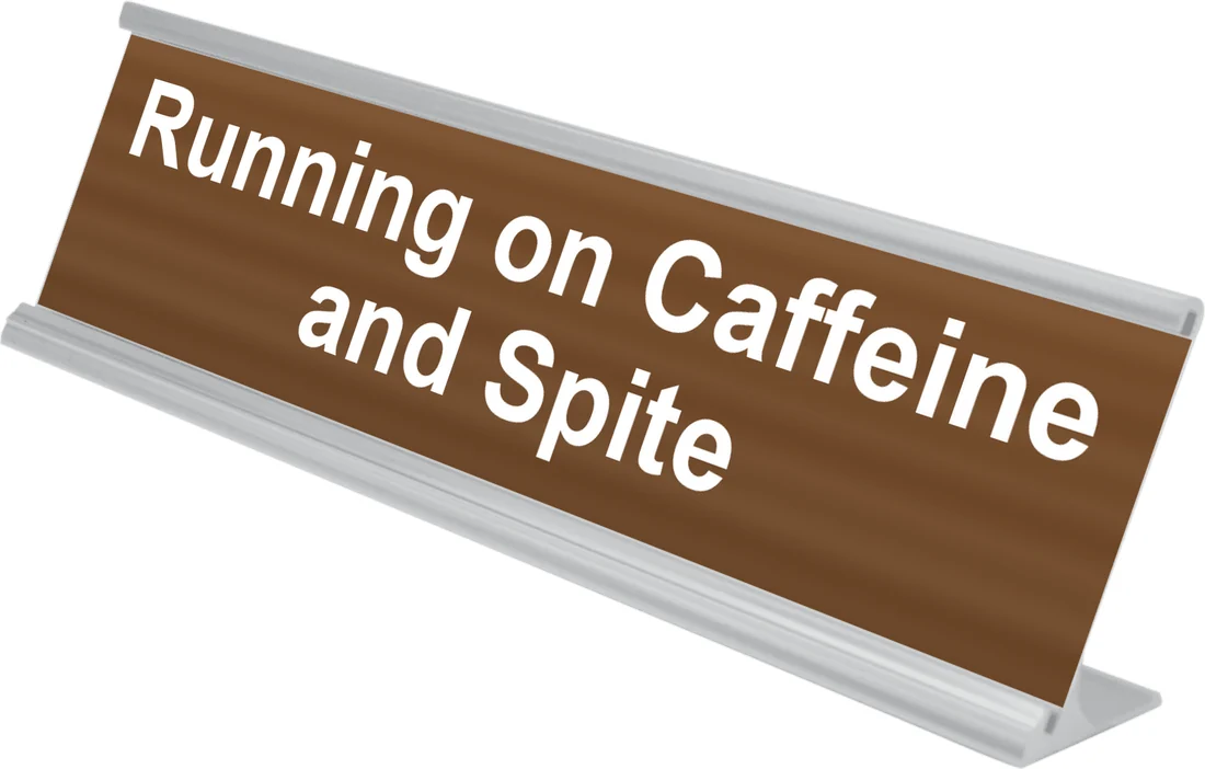 Running on Caffeine and Spite desk plate in walnut, shown in an aluminum desk holder