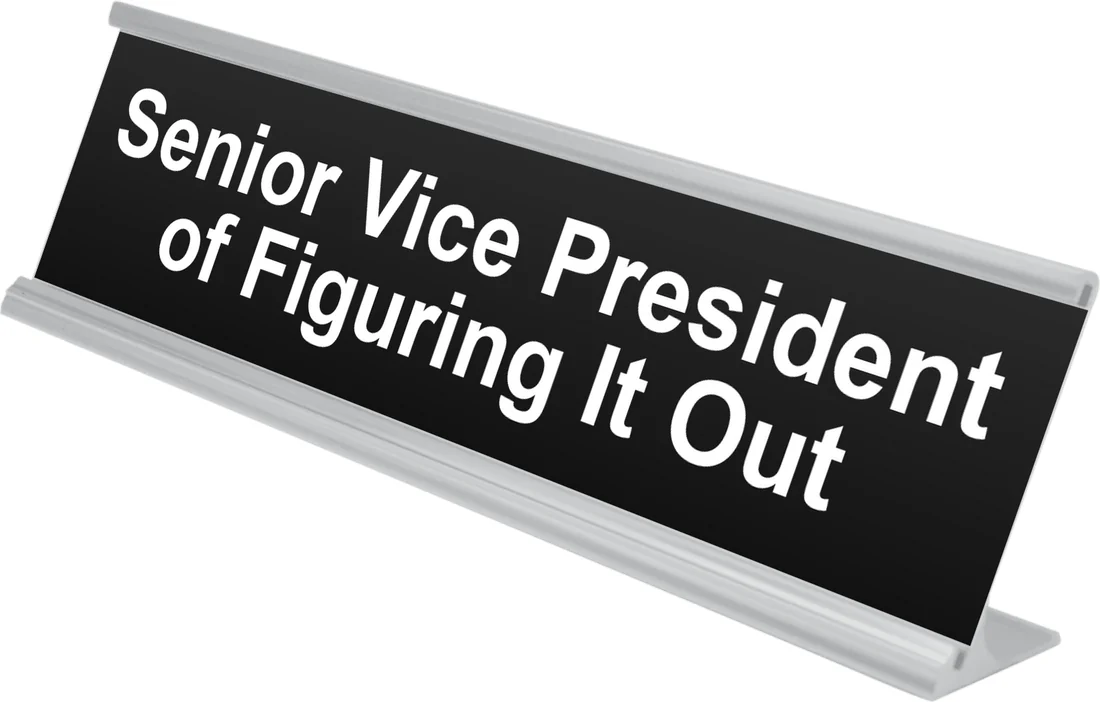 Senior Vice President of Figuring It Out desk plate in black, shown in an aluminum desk holder