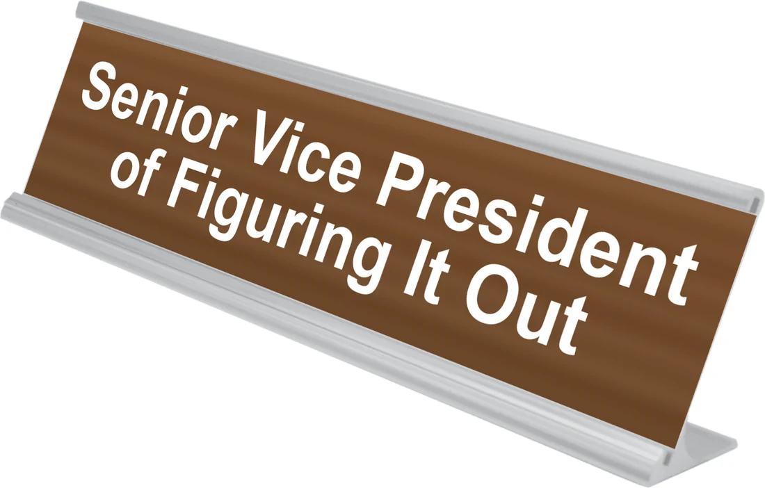 Senior Vice President of Figuring It Out desk plate in walnut, shown in an aluminum desk holder