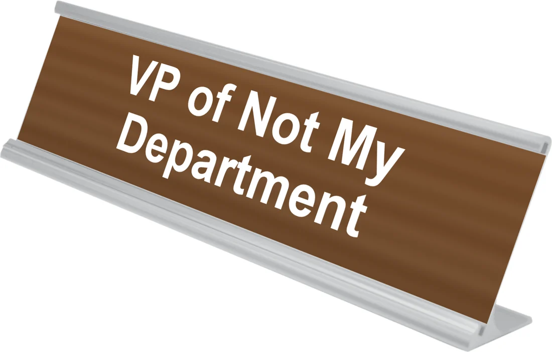 VP of Not My Department desk plate in walnut, shown in an aluminum desk holder